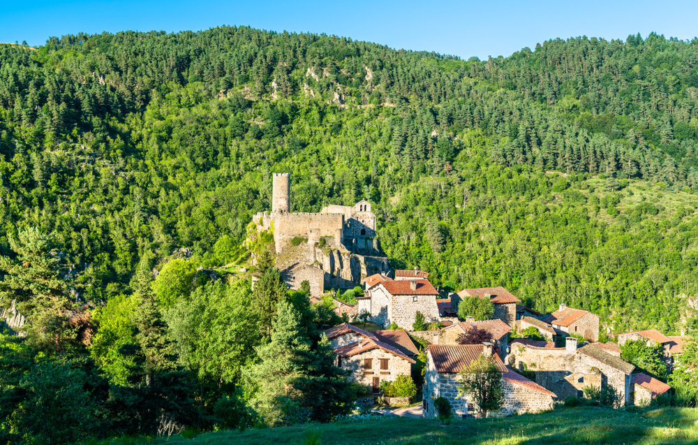Granieten huizen met rode daken en een stenen fort gelegen midden op een berghelling tussen de groene bossen.