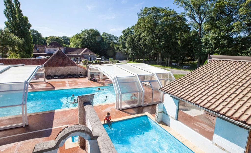 kindje dat aan de rand van een buitenzwembad zit en en kinderen die zwemen in een deels overdekt zwembad op Camping Castel La Bien Assise