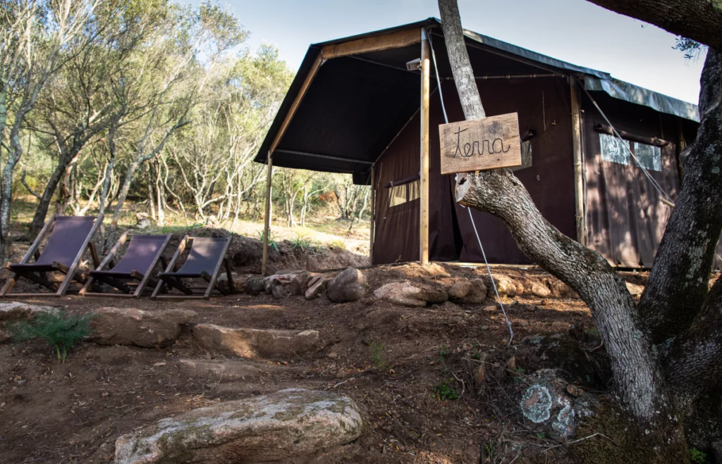 een bruine, dichte safaritent met daarvoor drie bruine strandstoelen en een boomstam met een bordje met het opschrift 'terra'
