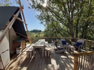 terras van een safaritent met tuinmeubilair en een buitenkeuken en uitzicht op een groene heuvel op Camping Les Arches in de Ardèche